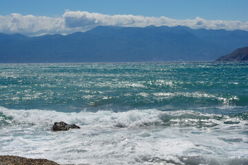 A view of the Adriatic Sea from beach in Baska on Island Krk featuring waves crashing against the shore with the Velebit mountain range in the background