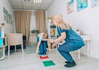 boy balancing on a red sensory mat while reaching for a card, session in bright room with...