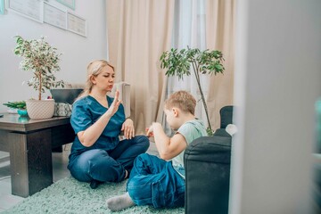 speech therapist engaging with young boy in nonverbal communication training, living room with warm...