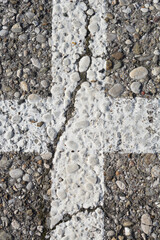 A close-up view of white crossed lines painted on an asphalt surface covered with small stones