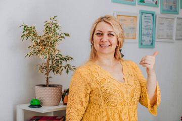 cheerful woman in yellow giving thumbs up in a bright office, concept of success coaching,...