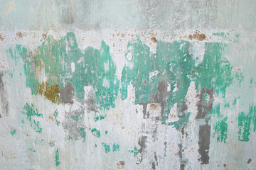 A deteriorated wall with peeling paint, exposed plaster, and rough texture. The different shades of gray, green, dark and white suggest areas of damage surface, decorate design background 
