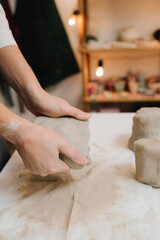 Hands of a female potter making ceramic clay product on the table in the pottery workshop. Potter is sculpting wet clay for ceramics products.