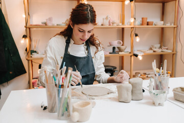 Woman artisan measures circle blanks for future ceramic plate. Preparation of clay before molding in the pottery wheel.