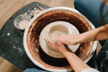 Craftswoman is molding porcelain dish in the pottery studio. Artisan sculpts a pottery plate on the...