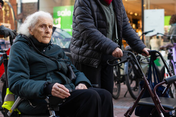 Obraz premium Mature woman walking with a walker next to elderly woman in wheelchair on the street
