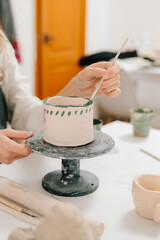 Artist is decorating and painting handmade ceramic clay cup in the creative workshop. Painter is...