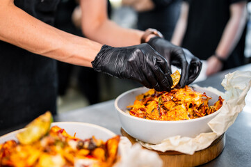 A close-up of a person wearing black gloves serving delicious nachos in a bowl. Freshly prepared with melted cheese and toppings, this dish is perfect for sharing. Ideal for food-related content.