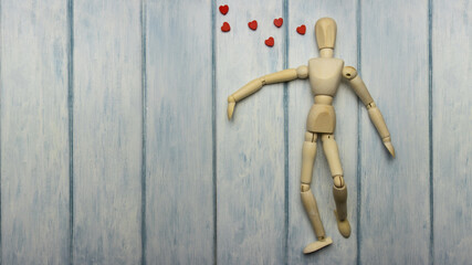 Wooden doll (model of a person) lies on a light wooden background and dreams of love. Holiday card for Valentine's Day.