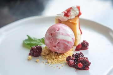 Berry ice cream served with cheesecake, crumbled biscuit, whipped cream and fresh berry on plate