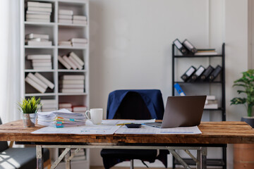 Laptop Computer, notebook, and eyeglasses sitting on a desk in a large open plan office space after working hours
