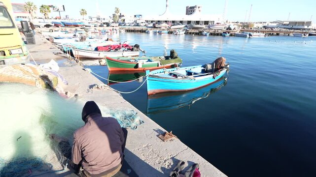 Harbor of Tripoli in Libya with fisherman fixing his net