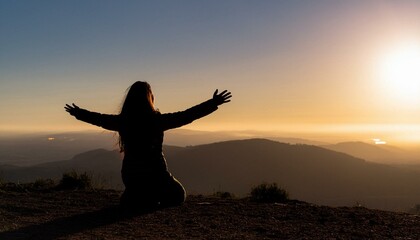 Fototapeta premium Silhouette of a person kneeling with open arms on a mountain peak, looking at the sky. Spiritual freedom and achievement concept with dramatic landscape, inspirational mood and copy space.