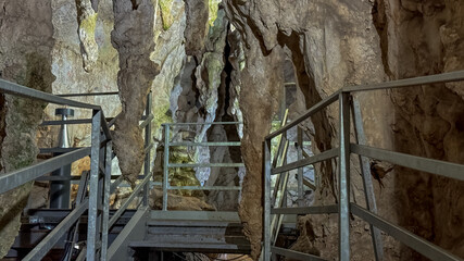 A rugged metal walkway leads through stunning stalactites in a dimly lit limestone cave, ideal for...