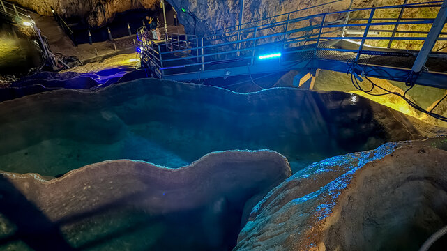 A vibrant cave interior with turquoise water and railings under blue lights, symbolizing adventure and exploration tourism  stopica pecina