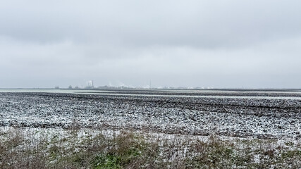 Sparse snow dusts a barren field under overcast skies, capturing winter's onset and agricultural...