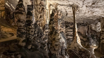 Majestic stalactites and stalagmites decorate a dimly lit limestone cave, symbolizing natural geological formations and adventure tourism exploration