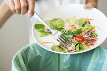 Compost from leftover food asian young housekeeper woman, female hand holding salad bowl use fork scraping waste, rotten vegetable throwing away into garbage, trash or bin. Environmentally responsible