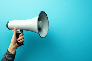 A hand holding a megaphone against a blue background with ample space for text or design. The human hand grips a loudspeaker, evoking a concept of noise music and shouting. 
