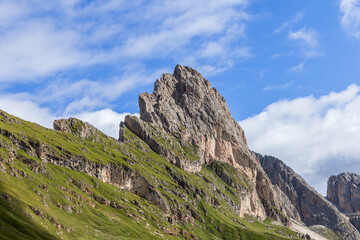 The jagged cliffs of Seceda stand out against the vibrant green hills, with intricate rock textures highlighted by sunlight under a clear alpine sky