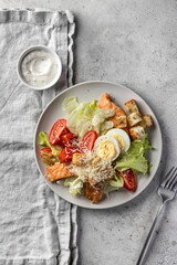 Caesar salad with chicken meat, green iceberg salad, eggs, tomatoes and parmesan cheese on gray background. Top view, flat lay