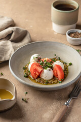 Caprese salad with fresh mozzarella and sliced tomatoes, served with micro greens and pesto sauce on beige background. Italian food
