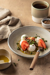 Caprese salad with fresh mozzarella and sliced tomatoes, served with micro greens and pesto sauce on beige background. Italian food