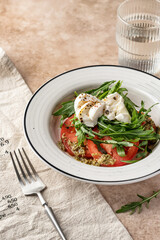 Caprese salad with fresh mozzarella, sliced tomatoes, aragula and pesto sauce served in white plate on beige background. Italian food, antipasti