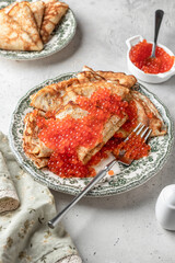 Pancakes or crepes with red caviar on a plate on white texrured background. Blini for Maslenitsa, recipe