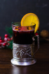 Delicious mulled wine with orange, cinnamon and honey in a glass with a vintage coaster on a dark...
