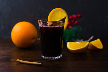 Delicious mulled wine with orange, cinnamon and honey in a glass on a dark background. Concept of a...