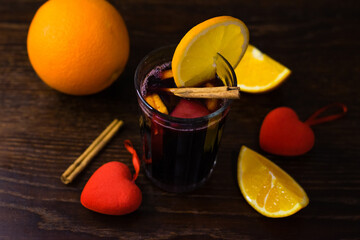 Delicious mulled wine with orange, cinnamon and honey in a glass and decorative red hearts on a...