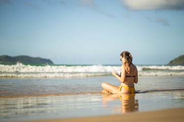 girl enjoys reading by the shore, with gentle waves lapping around them and a bright, blue sky in the background, creating a peaceful, inviting atmosphere.