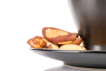 Brazil nuts without shells on a black ceramic saucer, macro, on a white background.