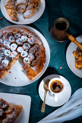 Traditional homemade banana caramel pie. French Tarte Tatin on a white plate with Turkish coffee on a green, emerald background.Top view