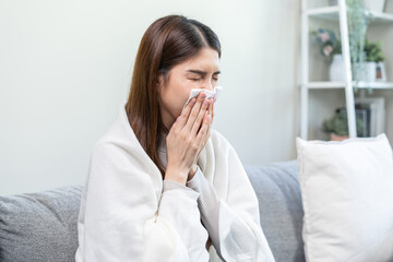 Sick, coronavirus or covid, tired asian young woman have a fever, flu and hand in use tissues paper sneezing nose, runny while sitting on sofa, couch at home. Health care with disease, pandemic virus