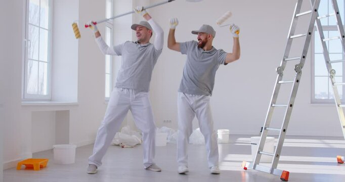 Team of house painters holding paint rollers and having fun painting the wall of new apartment. Building contractors doing repair renovation preparing to move. Renovating concept. 4k video.