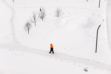 Worker in an orange jacket standing on a snowy path in winter, top-down view