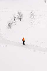 Worker in an orange jacket standing on a snowy path in winter, top-down view