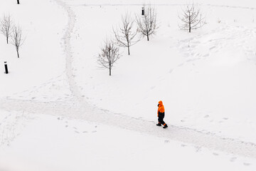 Worker in an orange jacket standing on a snowy path in winter, top-down view