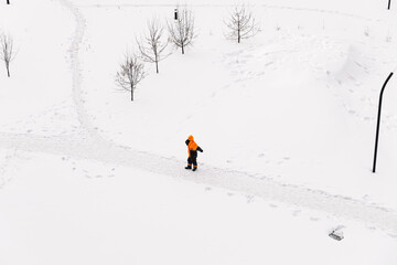 Worker in an orange jacket standing on a snowy path in winter, top-down view