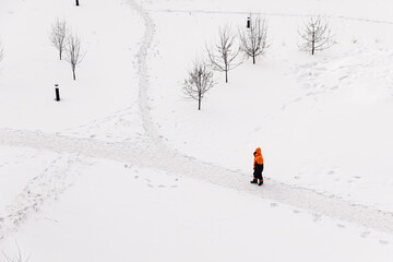Worker in an orange jacket standing on a snowy path in winter, top-down view