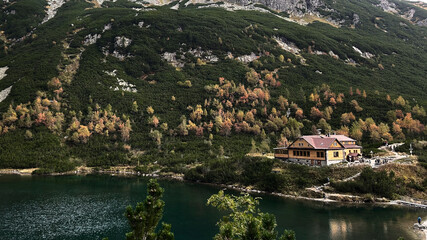 Fototapeta premium On the shore of a mountain lake there is a mountain hut that fits perfectly into the autumn forest landscape