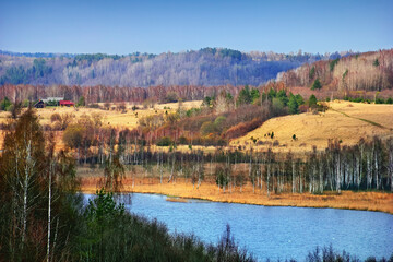 Beautiful view from Izborsk fortress, Pskov region, Russia. Rustic landscape - spring nature, fields with dry grass, river, trees (birch and spruce), few country houses at the background of blue sky