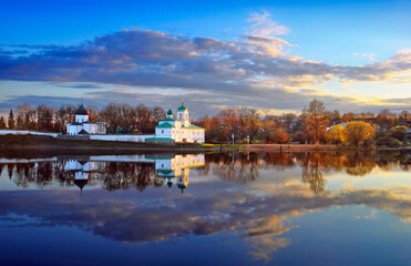 Fototapeta premium Pskov, Russia. Beautiful scenic view, Mirozhsky Monastery is a 12th-century Russian Orthodox monastery reflected at calm water of Pskova river at the background of cloudy sunset sky