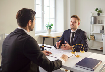 Confident lawyer in suit sitting at desk, discussing legal case with client in modern office....