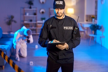Police officer wears uniform writing in crime reports form, gathering prosecution evidence at crime...