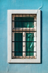 Obraz premium Old window with protective metal bars cage and white concrete frame on a blue wall