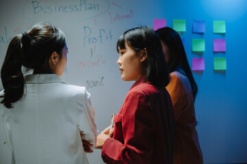 Businesswomen discussing business plan and profit in office meeting using whiteboard and sticky notes