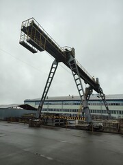 Gantry crane against the backdrop of an industrial landscape. A huge chimney with smoke pouring out of it. Post-apocalyptic landscape.
